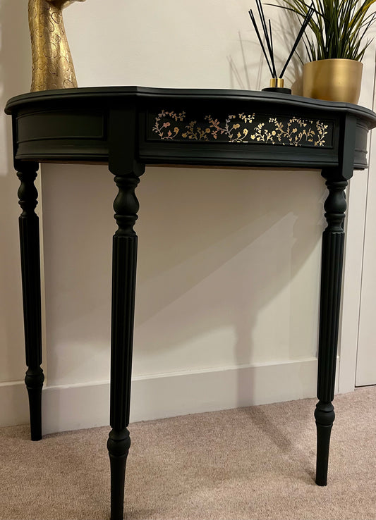 Black demi lune console table with decorative foil pattern on the drawer front.