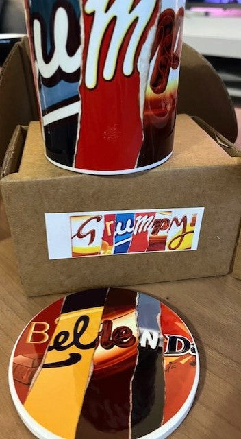 Colorful mug with Grumpy design standing on a cardboard box with a ceramic coaster with the word Bellend on.