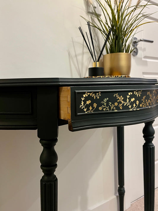 Decorative black console table with gold floral pattern on the front drawer which is slightly open
