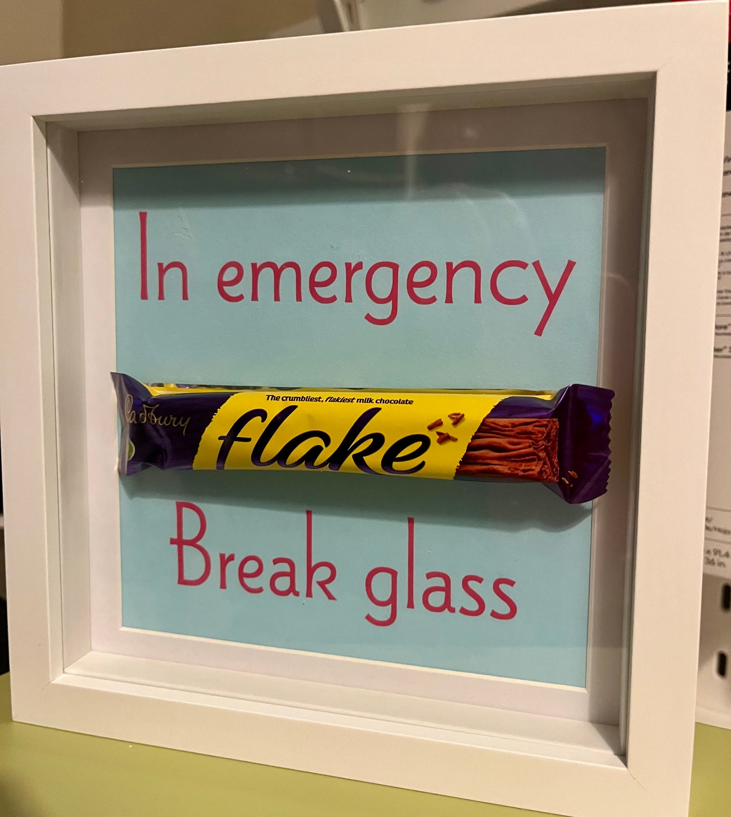 Framed candy bar with humorous text 'In emergency, break glass' on a light blue background
