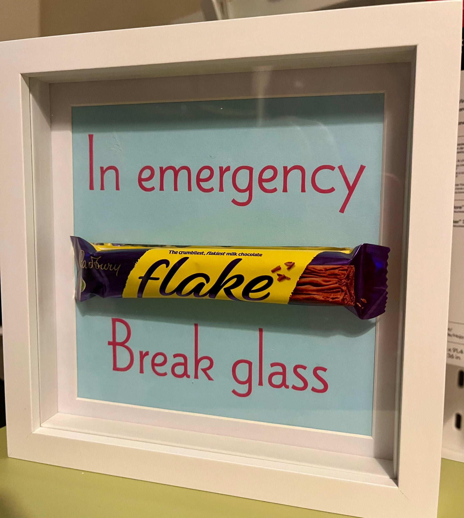Framed candy bar with humorous text 'In emergency, break glass' on a light blue background