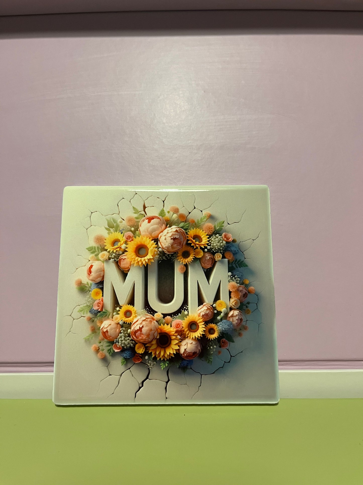 Decorative coaster with flowers and 'MUM' text on a cracked surface.