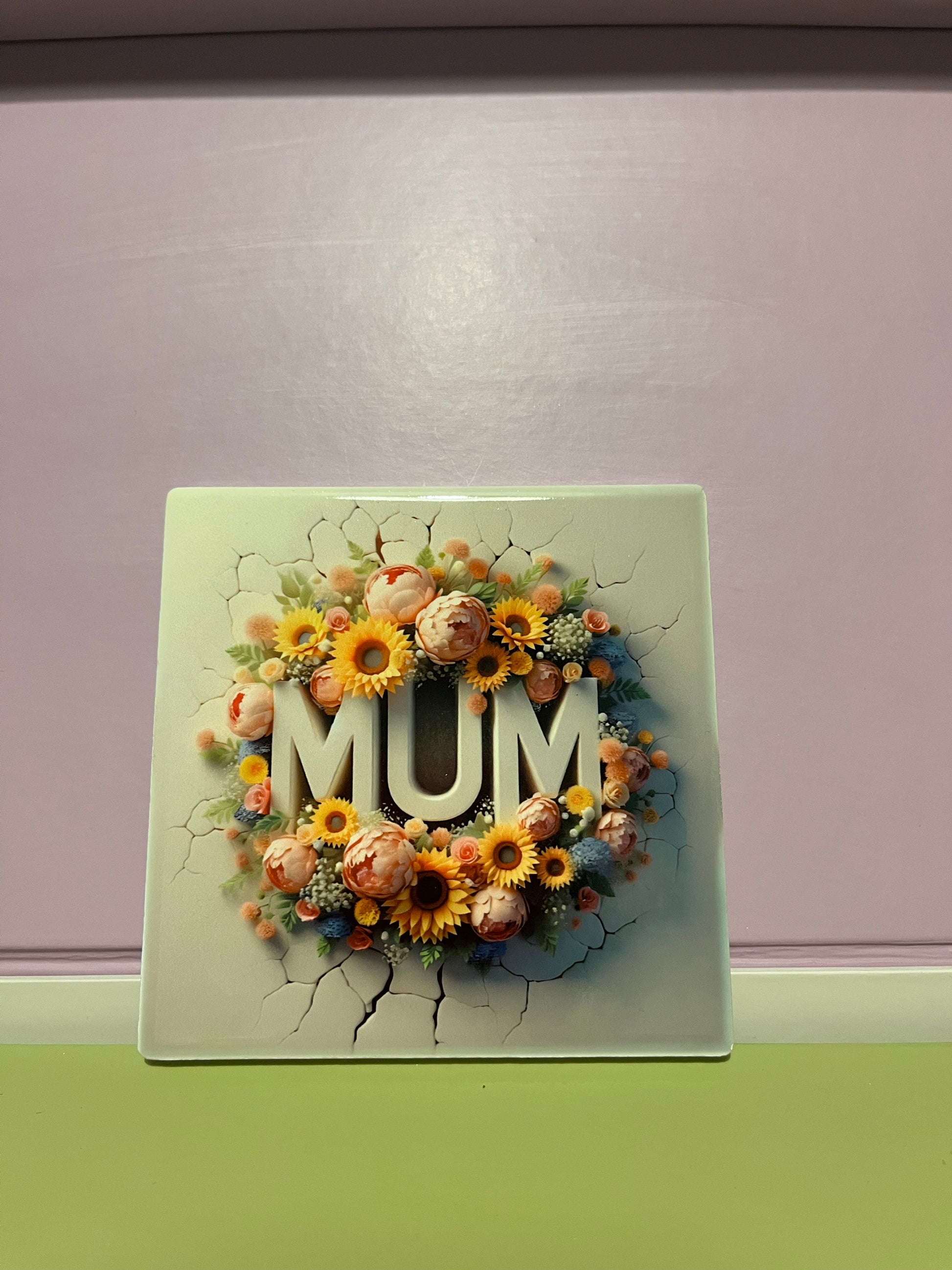 Decorative coaster with flowers and 'MUM' text on a cracked surface.