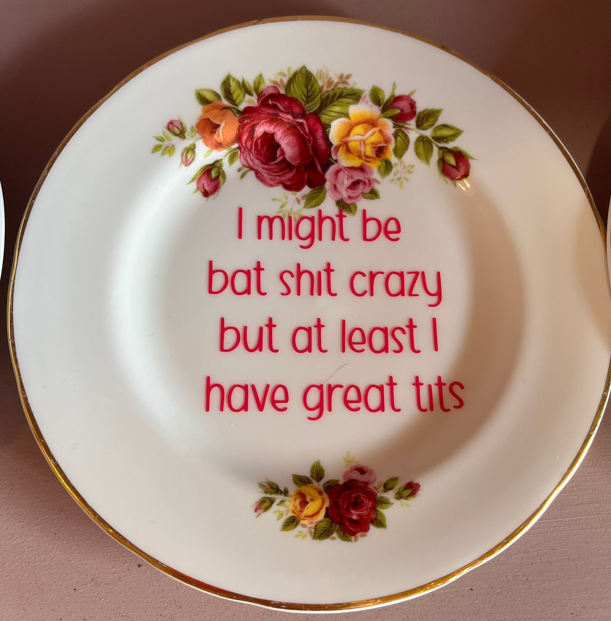 Decorative plate with floral design and humorous text on a pink surface