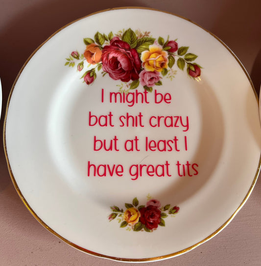 Decorative plate with floral design and humorous text on a pink surface