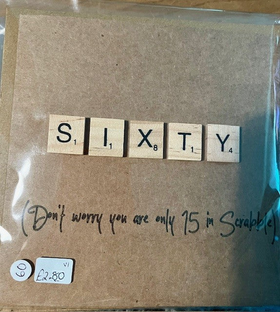 Card with 'SIXTY' spelled out using Scrabble tiles and a humorous note on a brown background.
